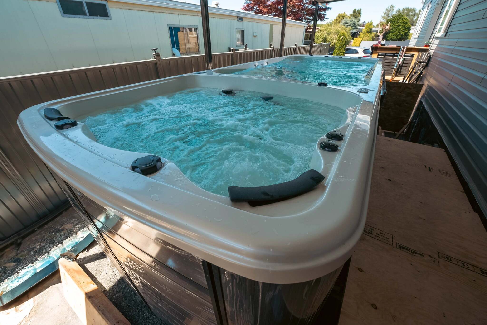 Two outdoor hot tubs with bubbling blue water, positioned on a wooden deck between houses.