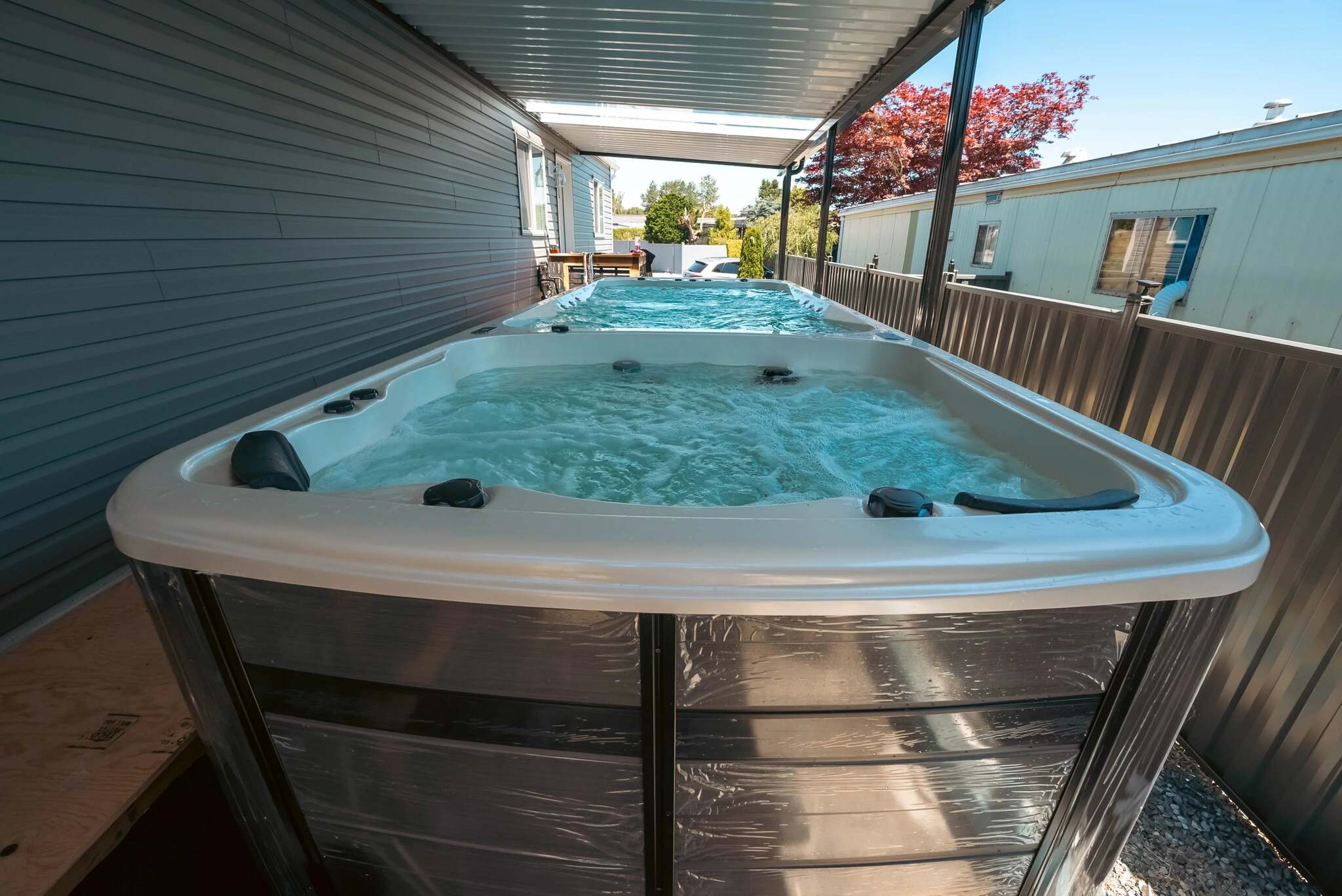 Two outdoor hot tubs with bubbling water under a covered patio, with a wooden fence and residential buildings in the background.